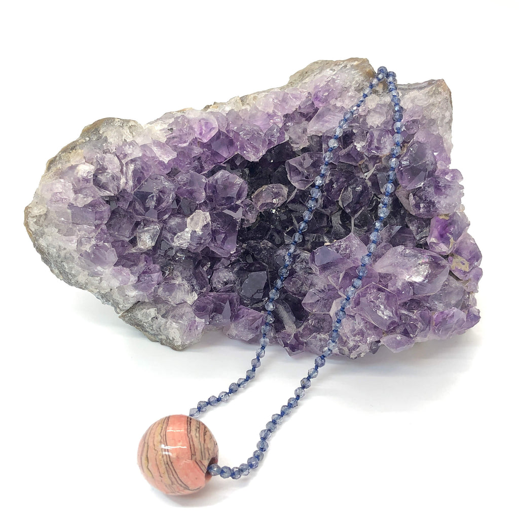 knotted iolite necklace with pink marbled paper bead charm shown draped on crystal