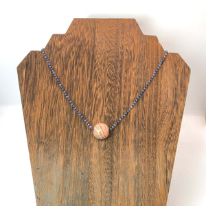 knotted iolite necklace with pink marbled paper bead charm shown on wooden necklace display