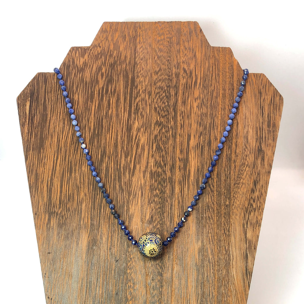 knotted sodalite bead necklace with handmade bead charm shown on wooden necklace display