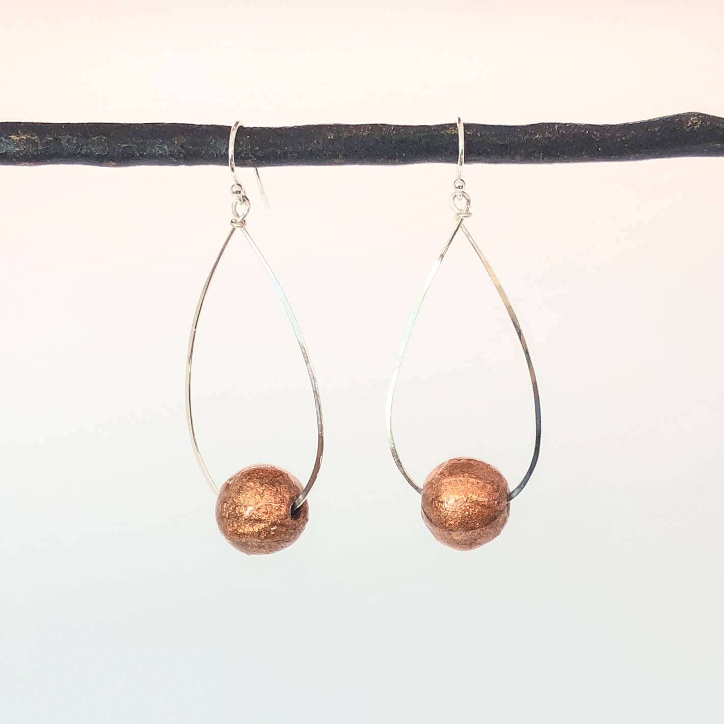 Sterling silver hammered teardrop dangle hoops with sparkly rose gold paper bead on white background