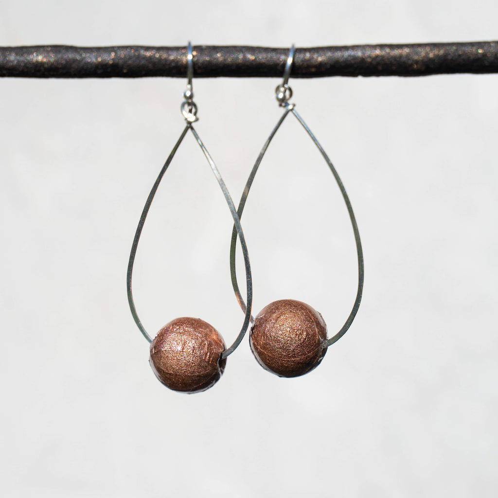 Sterling silver hammered teardrop dangle hoops with sparkly rose gold paper bead on display