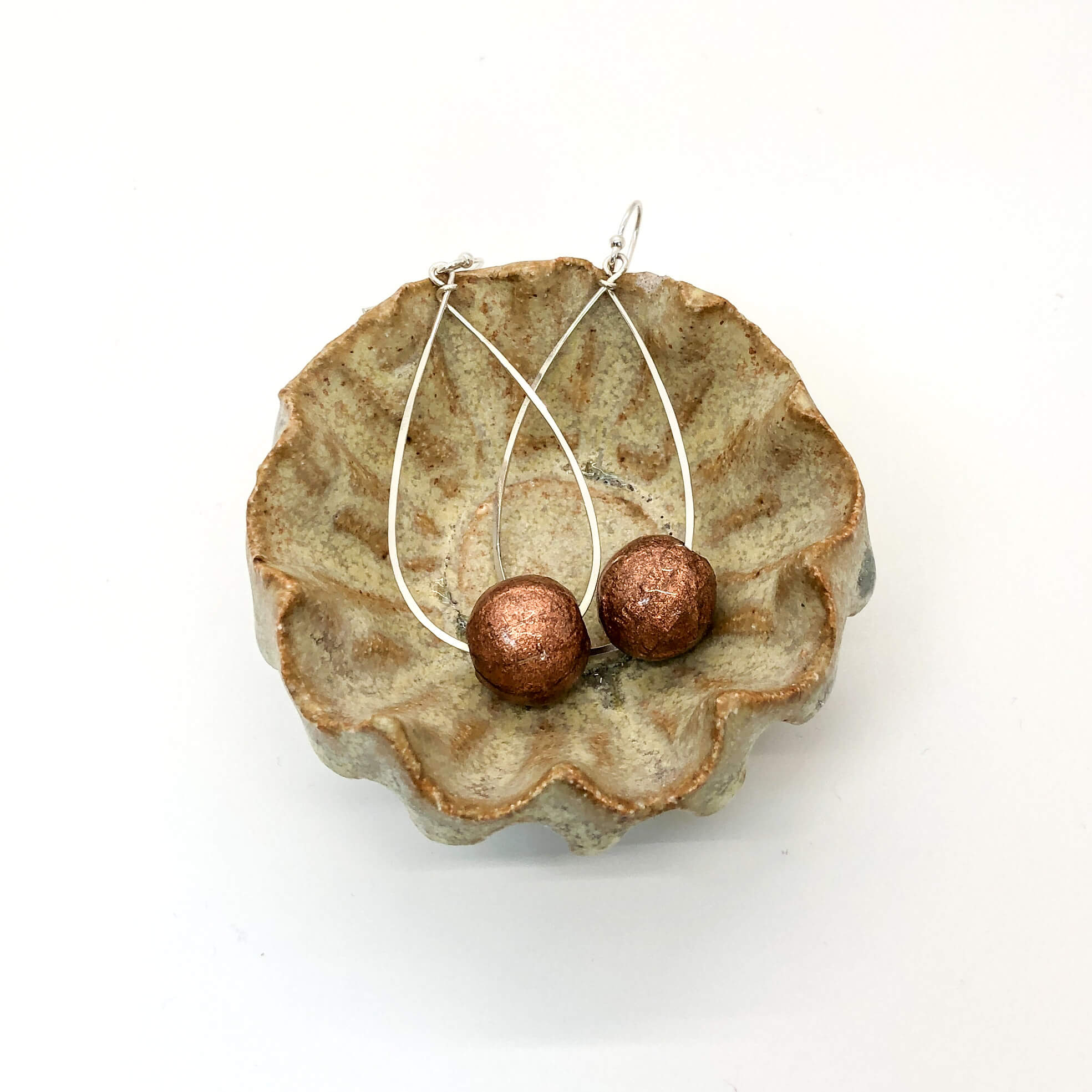 Sterling silver hammered teardrop dangle hoops with sparkly rose gold paper beads shown in ceramic dish
